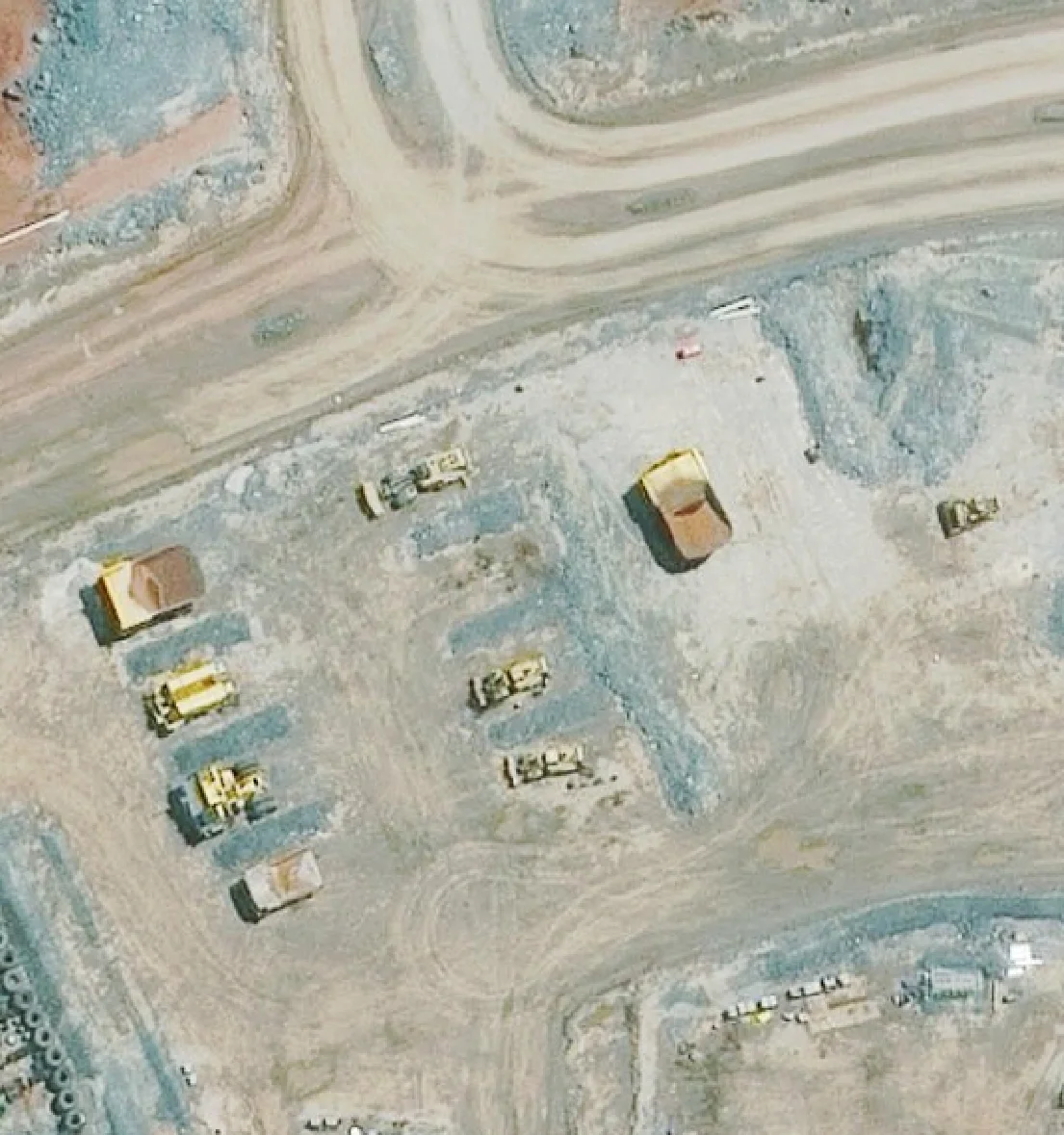 30cm satellite image of a mine equipment laydown beside a haul road, with haul trucks and dozers parked in rows