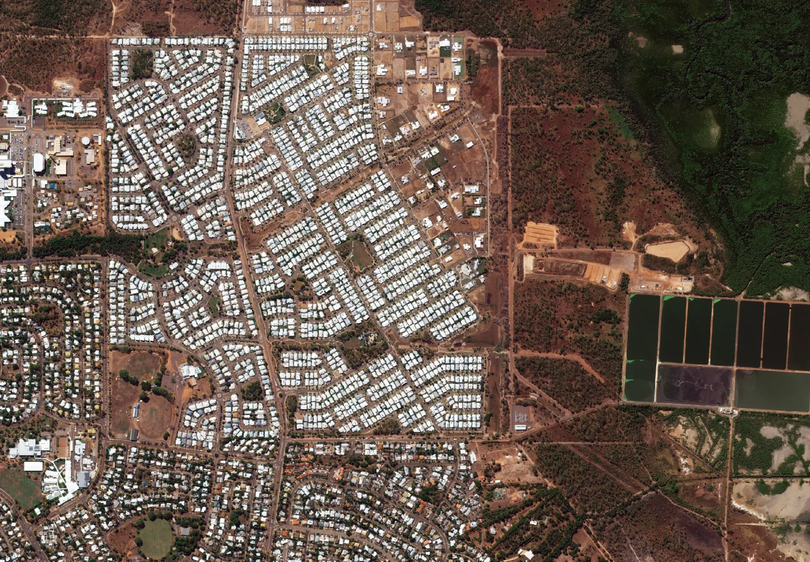 High-resolution satellite image of an Australian town showing individual house roofs, street layouts, a new subdivision under construction and treatment ponds