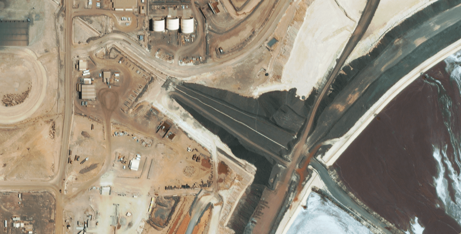 High-resolution satellite imagery of mine site infrastructure showing buildings and surface features.